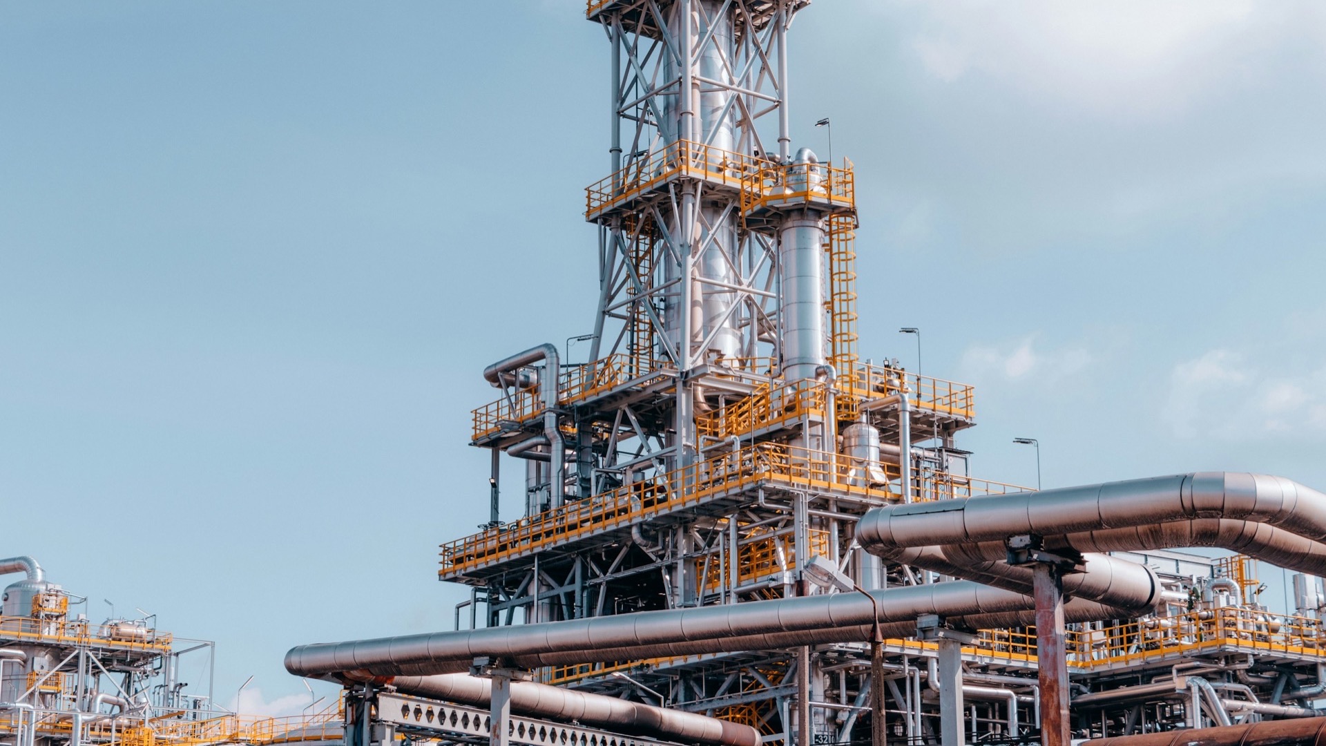 Refinery distillation tower and pipework under a clear blue sky